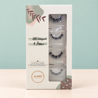 Stehende Glashes Full Glam Box mit vier Volumen-Wimpernpaaren vor salbeigrünem Hintergrund