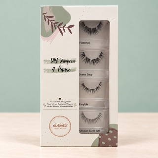 Stehende Glashes Soft Glam Box mit vier Dolleye-Wimpernpaaren vor salbeigrünem Hintergrund